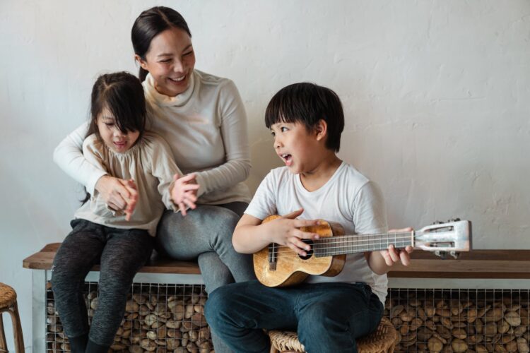 ethnic boy playing ukulele while sitting with mother and sister